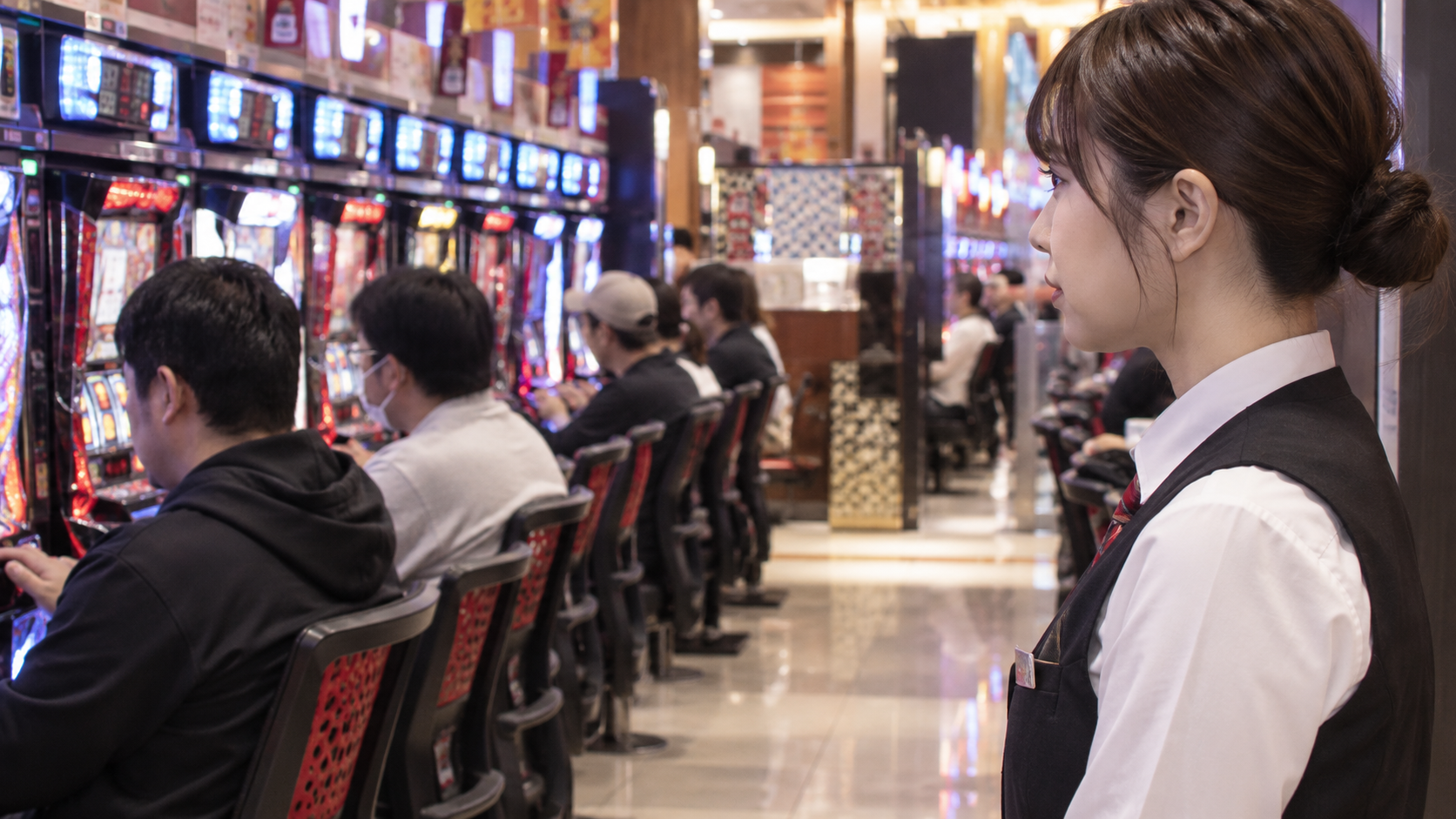通路から遊技席の様子に視線を向けるホールスタッフのイメージ